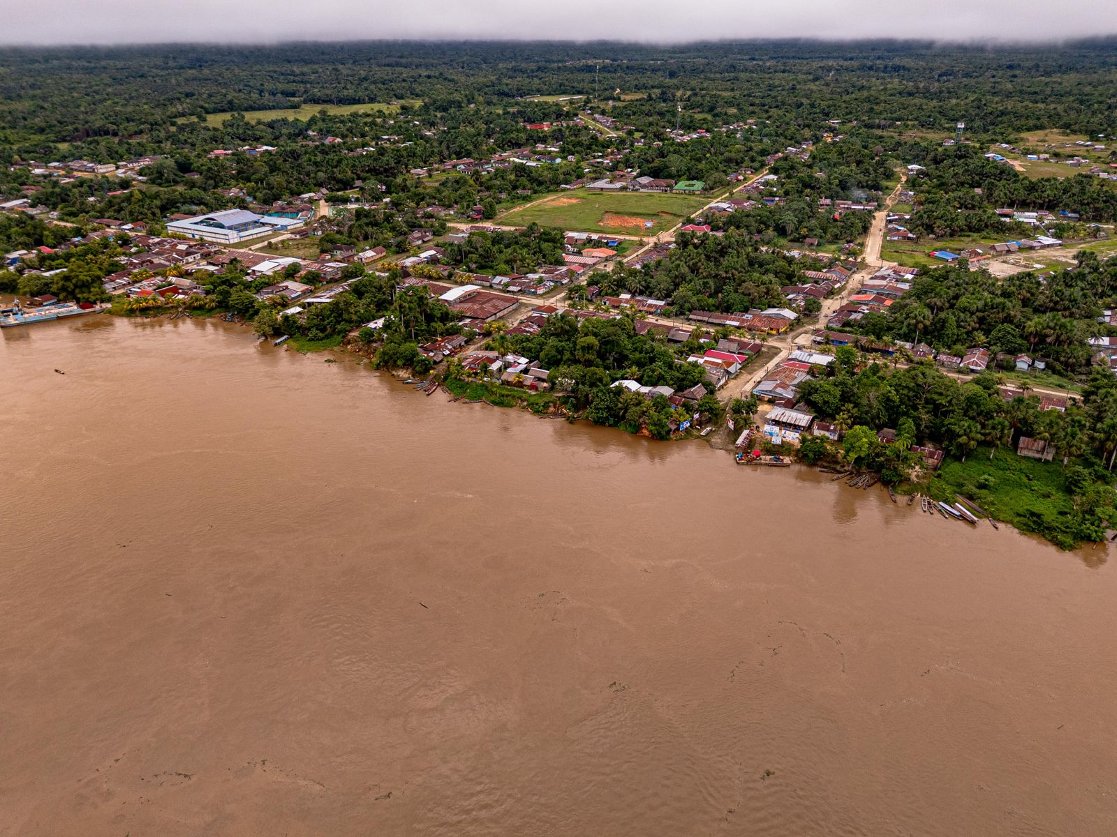 A riverside community on a wide brown river, forest behind it
